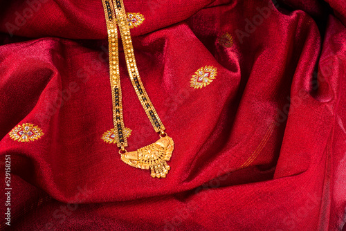 Mangalsutra or Golden Necklace to wear by a married hindu women, arranged with traditional saree with haldi, kumkum and flowers on plate.