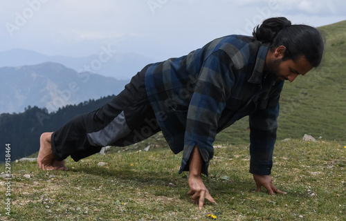 Full length of a Indian young man with ponytail hair doing three finger push ups in the top of mountain photo