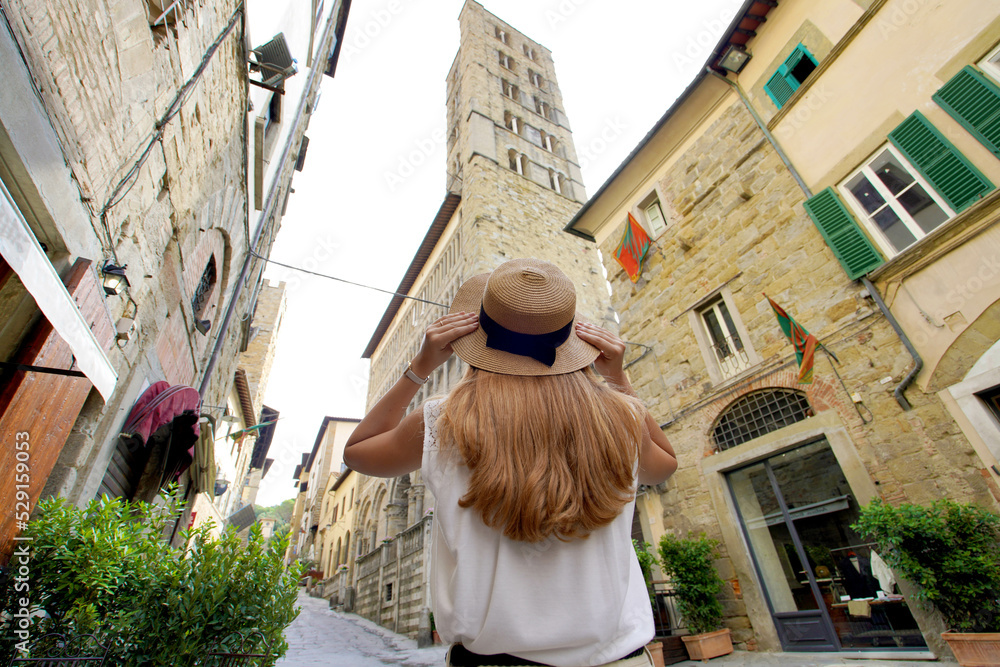 Beautiful tourist girl holds hat walking in the middle ages town of Arezzo, Tuscany, Italy. Low angle.