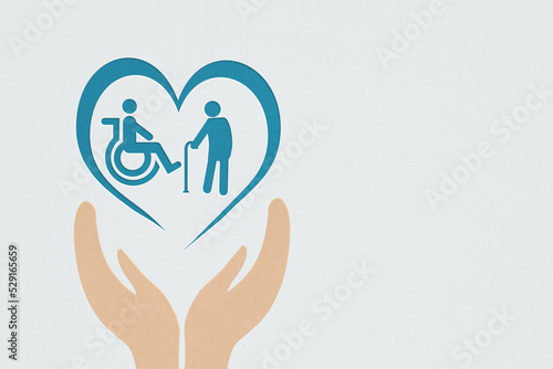 disabled person and elderly in heart paper cut over hands on grey background for wellness, wellbeing, nursing care concept