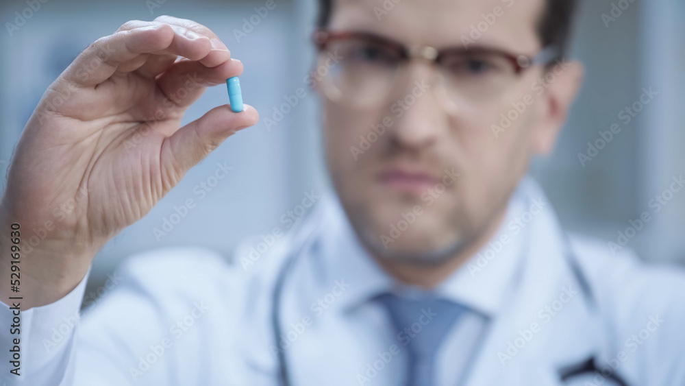 blurred doctor in glasses and white coat looking at camera and holding capsule. blurred doctor in glasses and white coat looking at camera and holding capsule.