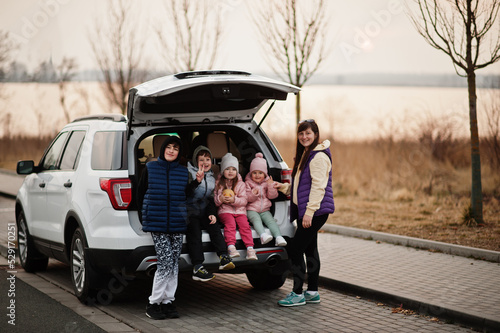 Mother with four kids sitting in trunk of big suv car. © AS Photo Family