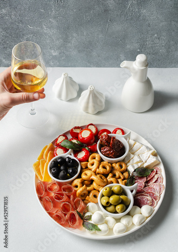 Classic italian antipasti or tapas  wine snacks set. Cheese variety, black and green olives, pickles, prosciutto di Parma, tomatoes, salami, tarallini, man hand taking glass of white wine. Copy space 