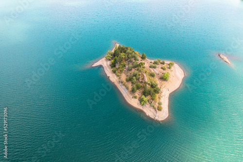 Small uninhabited, desert sand island with many trees in the middle of sea. Drone view, aerial view, top view