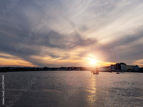 Silhouette of Galway hooker type wooden boat sailing from harbor at stunning sunset time. Hobby and water sport. Dark and moody sky and dark water of Galway bay, Ireland.