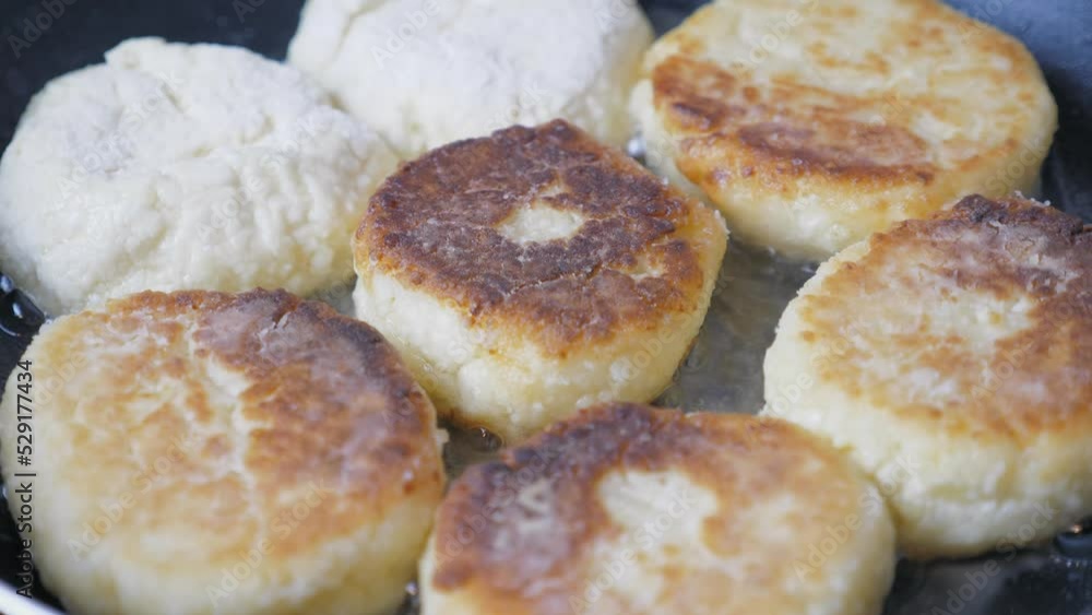 Many cheesecakes are fried in a frying pan on an electric stove. Breakfast preparation. Many cheesecakes are fried in a frying pan on an electric stove. Breakfast preparation.