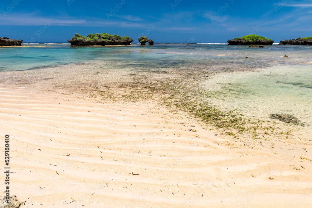 Paradise beach at low tide, crystal clear turquoise water, wavy sands, green islets, blue sky.