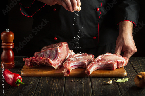 Professional chef sprinkles raw ribs with salt. The concept of cooking delicious food for the hotel
