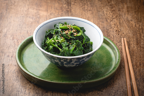 Spinach Ohitashi  or Japanese Spinach Salad  in a dashi-based sauce  on the wooden background. Umami flavor. Vegetarian recipes Yasai. Aesthetic composition and authentic Japanes ceramic