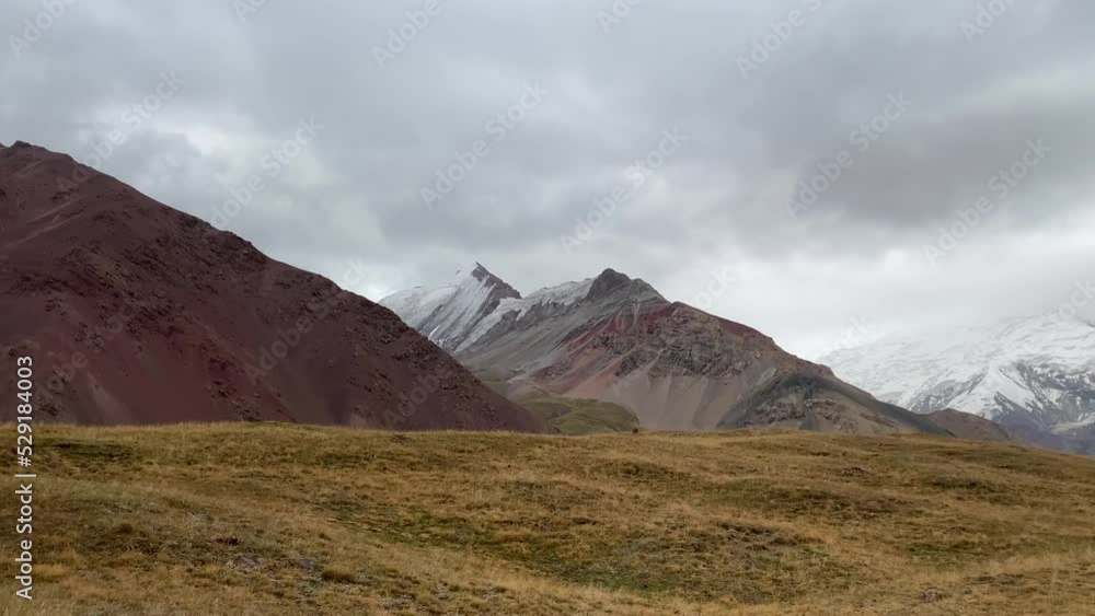 The amazing nature of Kyrgyzstan. Beautiful colored powerful mountains, snow-capped peaks and green fields. Cloudy sky over the Base Camp under Lenin Peak.