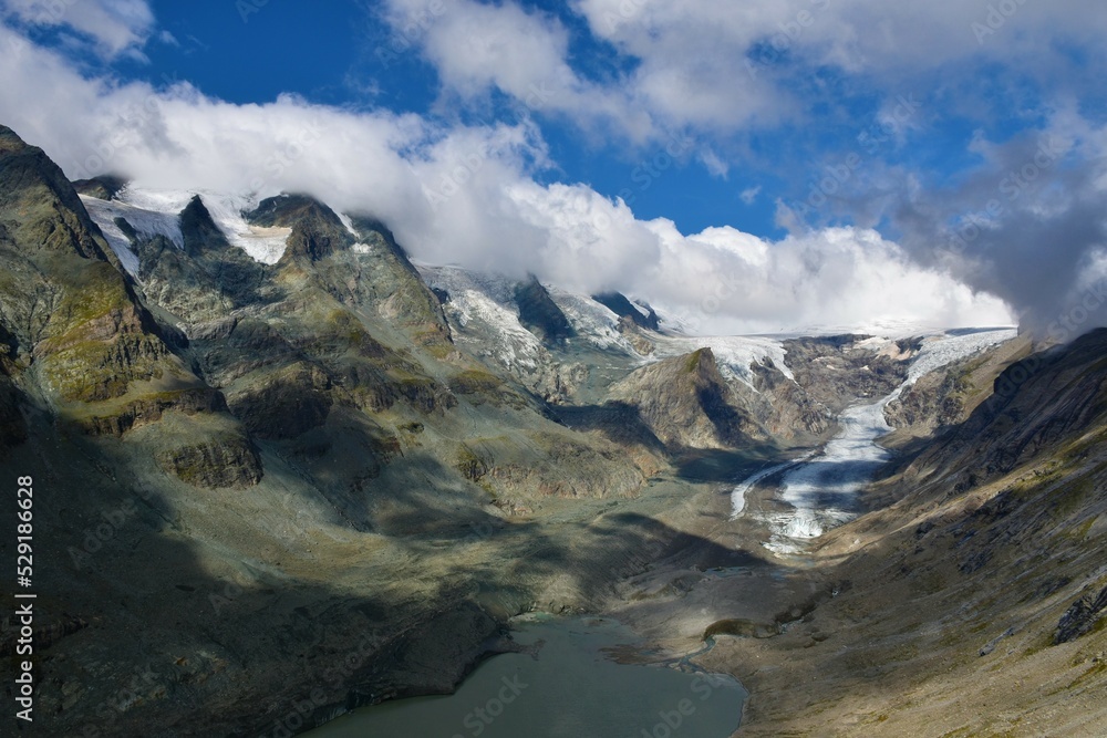 Scenic view of Pasterze Glacier and mountains of the Glockner Group in High Tauern in Austrian Central Alps, Carinthia, Austria with the peaks in clouds and blue sky above