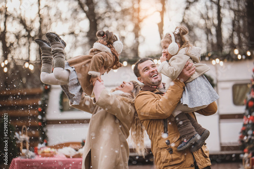 happy family of four: mom, dad and twin sisters celebrate Christmas near trailer with New Year decorations. Stylish family in fur coats and sheepskin coats is having fun in the snow. Selected focus