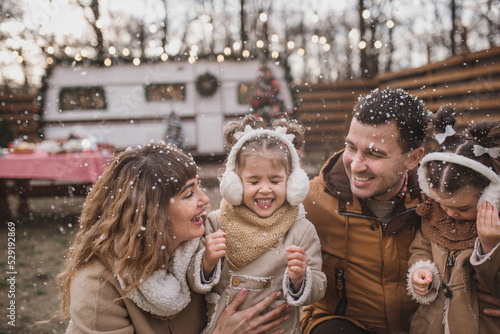 happy family of four: mom, dad and twin sisters celebrate Christmas near trailer with New Year decorations. Stylish family in fur coats and sheepskin coats is having fun in the snow. Selected focus