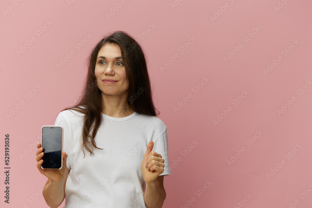 a beautiful, happy woman with long dark hair stands in a light t-shirt with a phone in her hands and shows a thumbs up a beautiful, happy woman with long dark hair stands in a light t-shirt with a phone in her hands and shows a thumbs up