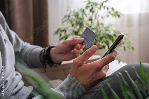 Young man makes shopping online on a smartphone, sends an online payment with a credit card. Close-up of male hands with phone and credit card