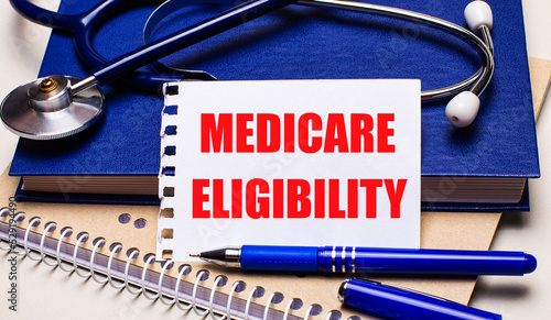 On the table are notepads, a stethoscope, a pen and a sheet of paper with the text MEDICARE ELIGIBILITY. Medical concept