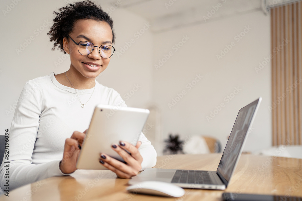 A female freelancer smiles at a video call, uses a laptop and tablet at the workplace in the office A female freelancer smiles at a video call, uses a laptop and tablet at the workplace in the office