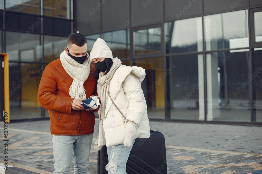 Couple standing outdoors wearing face mask and waiting for travel