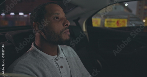 Tela A black man seated in car backseat commuting from work at night