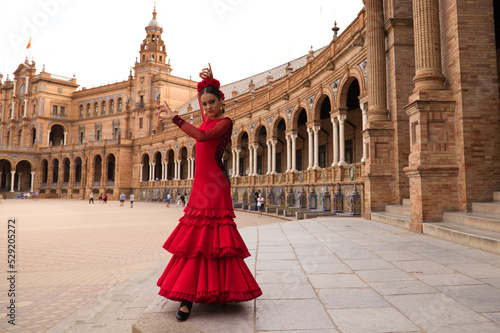 Beautiful teenage woman dancing flamenco in a square in Seville, Spain. She wears a red dress with ruffles and dances flamenco with a lot of art. Flamenco cultural heritage of humanity.