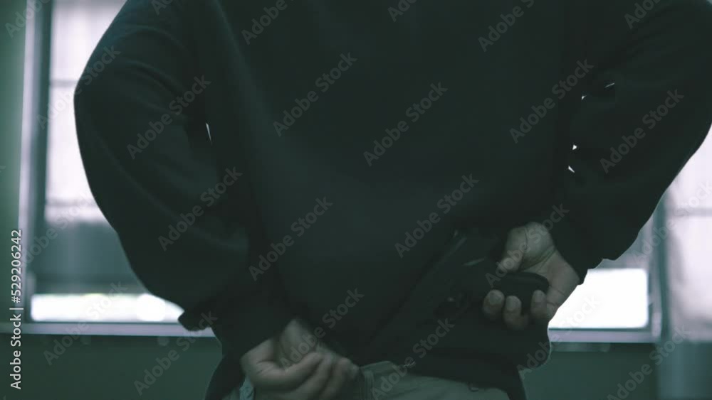 The male assassin put the gun in the rim of his pants, covered his hood, criminal man walking carefully over to look outside his eyes to see his target. The male assassin put the gun in the rim of his pants, covered his hood, criminal man walking carefully over to look outside his eyes to see his target.