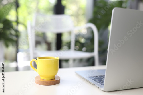 Laptop and yellow coffee cup on white table indoor work from home