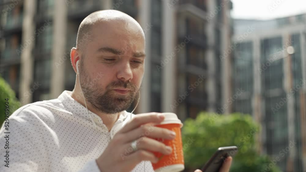 A businessman solves cases at lunch break while drinking coffee. A man is texting on the phone near the business center. High quality 4k footage A businessman solves cases at lunch break while drinking coffee. A man is texting on the phone near the business center. High quality 4k footage