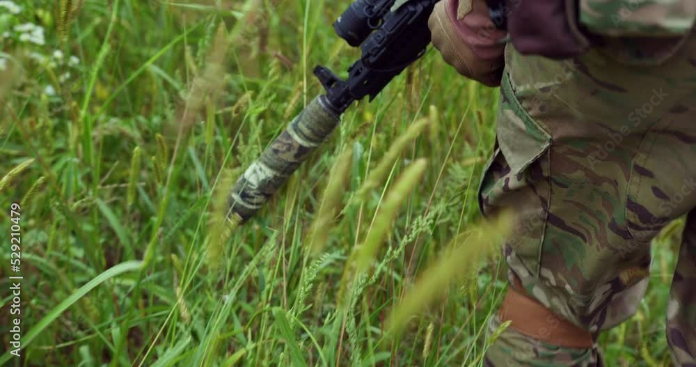 a soldier drives a silenced weapon across the grass. back view. Ukrainian soldier. close-up. sniper rifle on green grass. soldier steps a soldier drives a silenced weapon across the grass. back view. Ukrainian soldier. close-up. sniper rifle on green grass. soldier steps