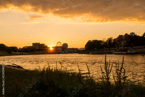 Sunset on the Vistula river in Krakow. Sun hides behind buiding and big wheel.