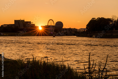 Sunset on the Vistula river in Krakow. Sun hides behind buiding and big wheel.