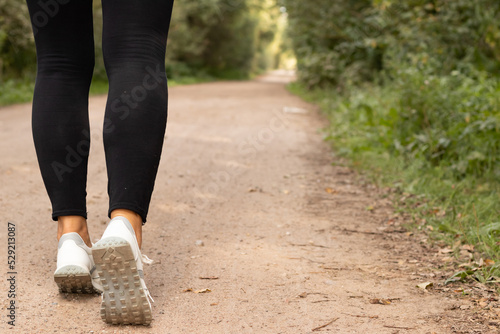 women's legs in black leggings and white sneakers on a jog in the woods Healthy lifestyle
