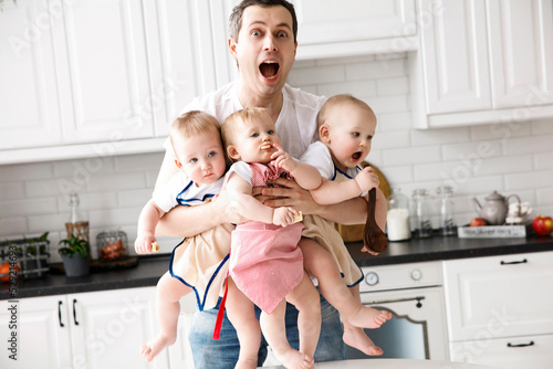triplets, two boys and a girl in the arms of a happy father. kitchen background