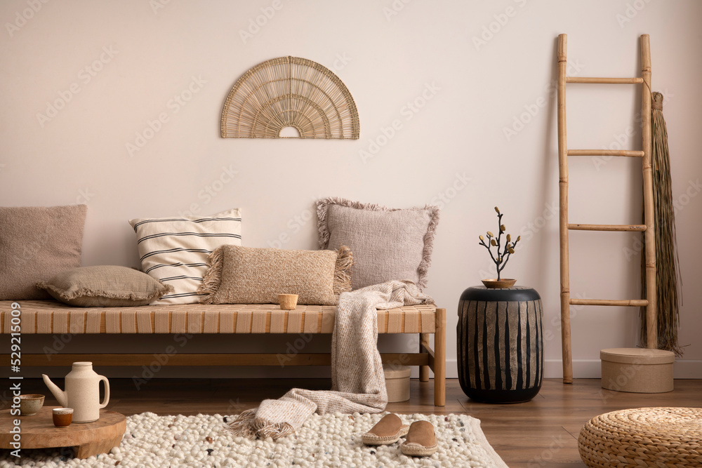 Boho and cozy interior of meditation room with beige chaise lounge, carpet,  rattan pouf, ladder, tea pot, side table, pillows, decoration, books and  personal accessories. Warm home decor. Template. Stock Photo