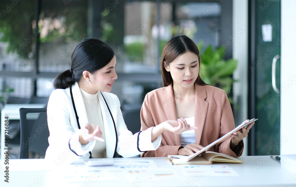 Two young Asian businesswoman discuss investment project working and planning strategy. Business people talking together with laptop computer at office. Two young Asian businesswoman discuss investment project working and planning strategy. Business people talking together with laptop computer at office.