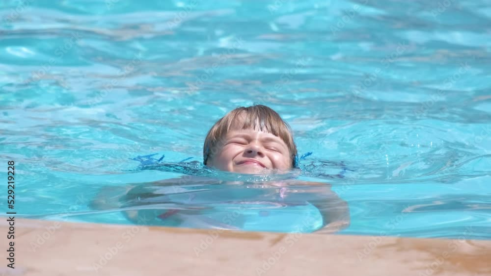 Child girl learns to swim. Funny face with closed eyes on bright blue rippled water surface Child girl learns to swim. Funny face with closed eyes on bright blue rippled water surface