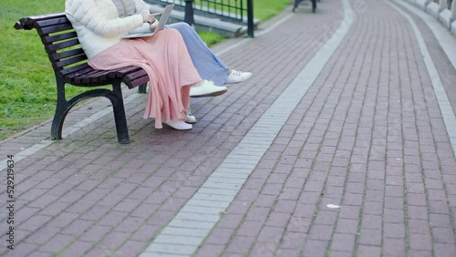 Wallpaper Mural two unrecognizable women sit park bench using laptop, female couple in long skirts talking searching websites computer outdoors. girlfriends spending time together in sunny cold day outside Torontodigital.ca