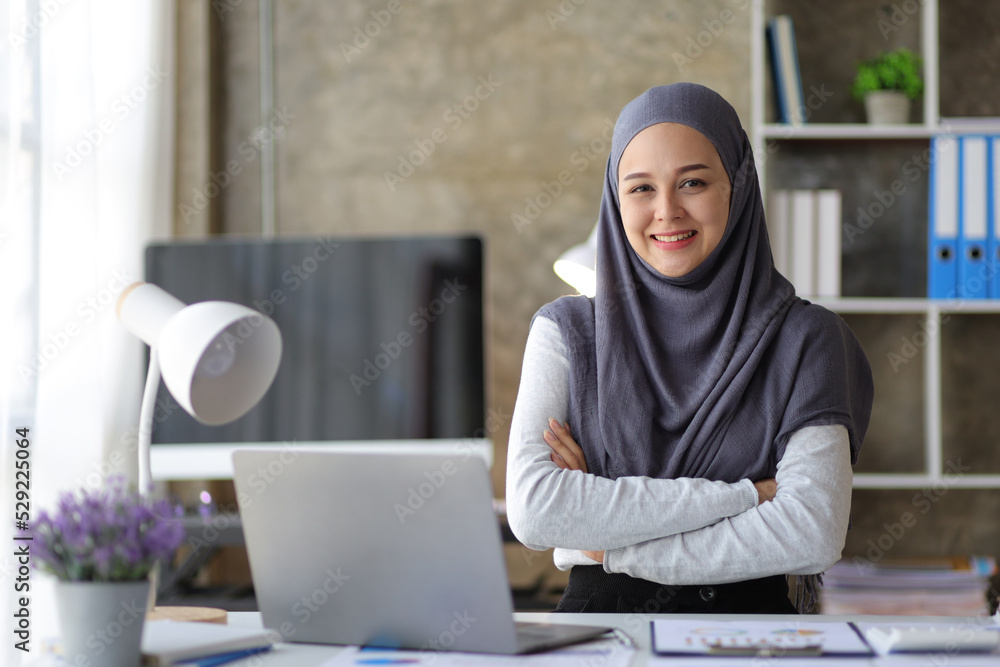 Portrait of a charming, smiling Muslim woman looking at the camera at her desk in the office. Portrait of a charming, smiling Muslim woman looking at the camera at her desk in the office.