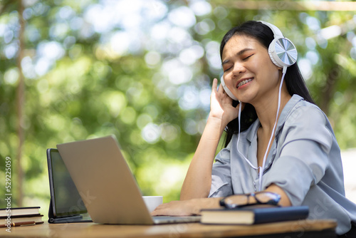 Outdoor woman using laptop listening to music enjoying wearing a headset.