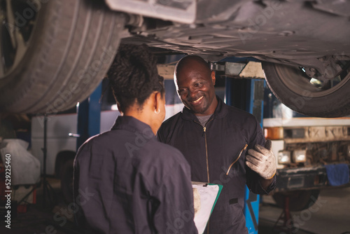 African american  Two mechanics - man examining car engine. Auto mechanic working in garage.Car Mechanic Detailed Vehicle Inspection. Auto Service Center Theme. © Montri