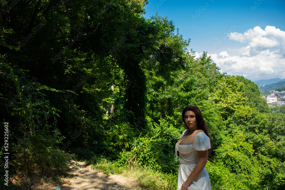 Beautiful black-haired girl in a white dress on a walk in her garden