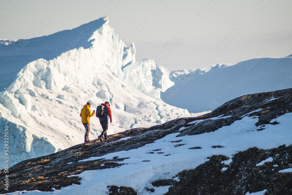 Tourists hiking on hills next to icebergs in winter, next to Ilulissat Icefiord in Greenland on sunny day