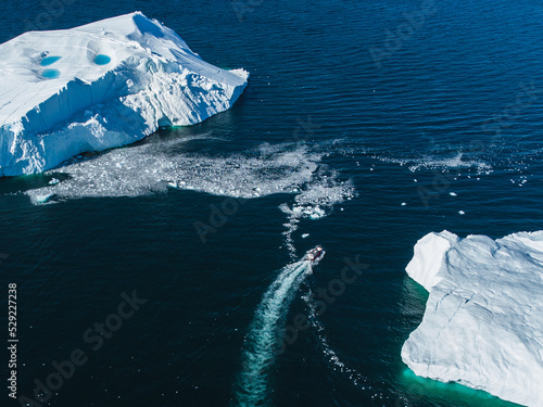 Boat on the sea in Greenland next to big icebergs close to Ilulissat icefiord, aerial view