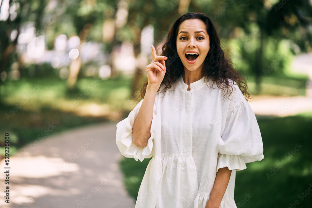 Cheerful curly-haired brunette girl with open mouth raises her index finger. Girl has an idea. High quality photo Cheerful curly-haired brunette girl with open mouth raises her index finger. Girl has an idea. High quality photo
