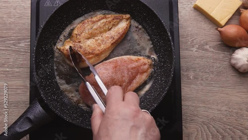Chicken fillet is fried in a pan in butter on a kitchen stove in the kitchen. The hand of the cook turns the fillet.