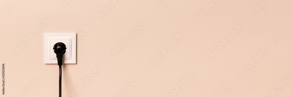 White european electrical outlet with black plug inserted into it on modern beige wall with copy space banner. Wide panoramic header White european electrical outlet with black plug inserted into it on modern beige wall with copy space banner. Wide panoramic header
