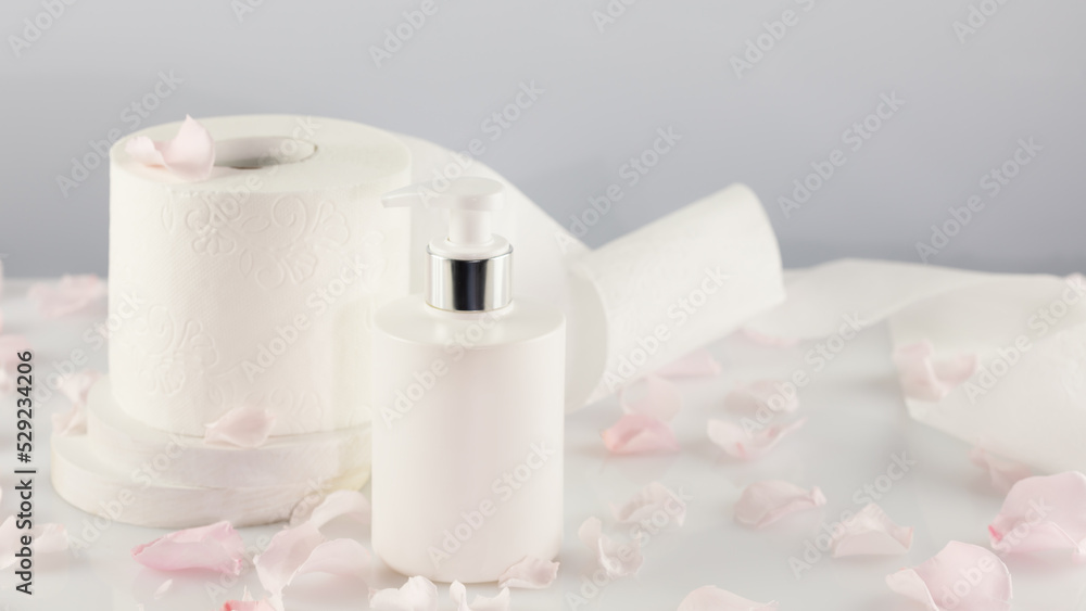 Roll of toilet paper with cosmetic dispenser bottle on light background with rose petals and copy space. White toilet tissue, Hygiene product. Restroom soft touch toilet paper. Soft focus style image Roll of toilet paper with cosmetic dispenser bottle on light background with rose petals and copy space. White toilet tissue, Hygiene product. Restroom soft touch toilet paper. Soft focus style image