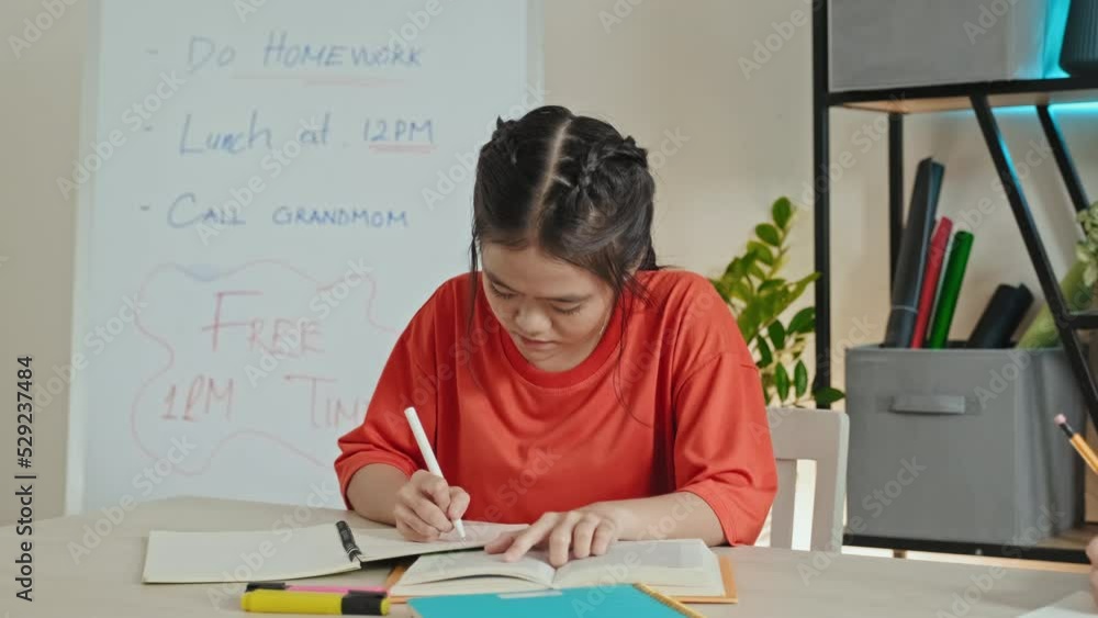 Asian girl reading textbook and taking notes at desk during school lesson in classroom Asian girl reading textbook and taking notes at desk during school lesson in classroom