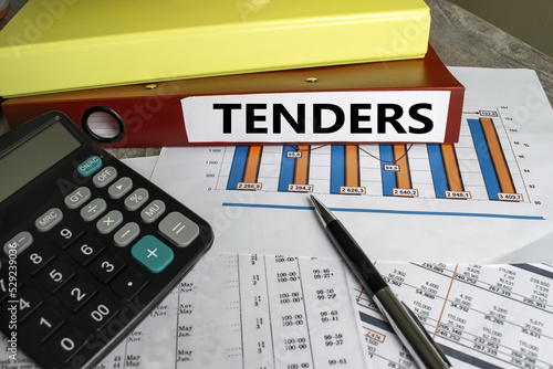 A red folder with the inscription tenders on financial documents with figures and a diagram.