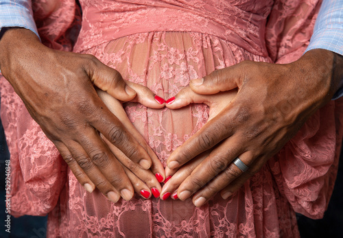Hands of young African American black couple forming a heart shape on the pregnant belly of the woman with man's hands on top showing love of mom and dad for unborn baby
