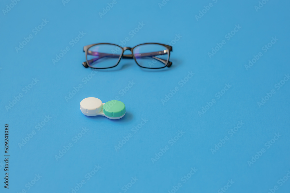 Glasses and a container for lenses on a blue background. Soft focus Glasses and a container for lenses on a blue background. Soft focus
